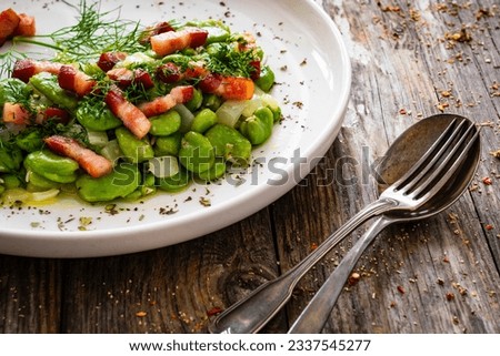Broad beans with garlic, dill and bacon on wooden table 