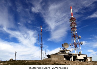 Broad perspective of a remote mountain communications center with different antennas and towers against a deep blue sky with beautiful white clouds
