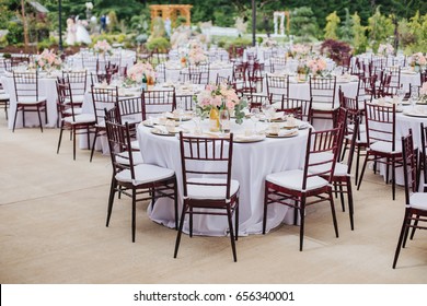Broad View Of The Outdoor Wedding Reception With Empty Tables And Wooden Chairs
