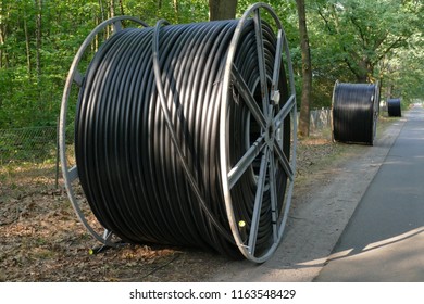 Broadband Cable Drum With Laying Trailer And Other Rolls With Black Fiber Optic Cables For Faster Internet In Rural Regions - In The Village Wedemark Brelingen, District Hanover, Germany