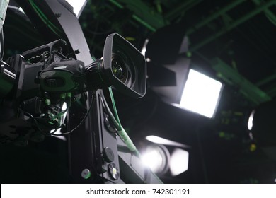 Broadcast studio camera on crane in green studio room with LED lights on the ceiling.