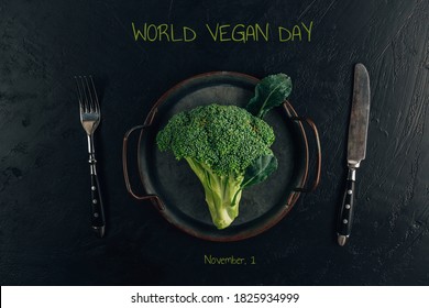 Broccoli and cutlery on a black background. The inscription "World Vegan Day". Top view
