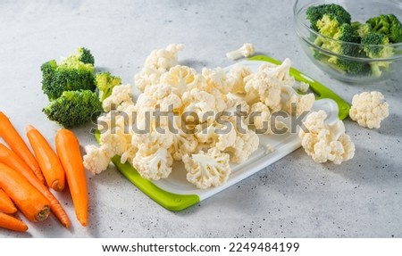 Broccoli florets, cauliflower, carrots close-up. Fresh raw organic vegetables on a white cutting board on kitchen table, still life, cooking process