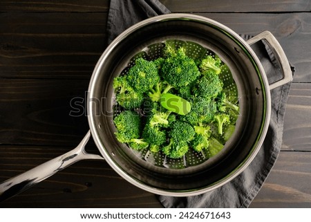 Broccoli Florets on a Steamer Basket Placed in a Saute Pan: Raw broccoli florets in a foldable metal steaming basket placed in a skillet with water