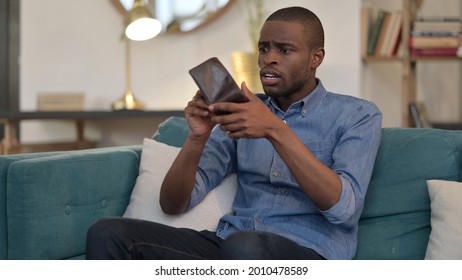 Broke Young African Man Checking Empty Wallet On Sofa 