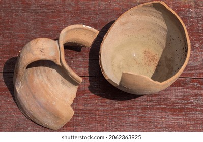 Broken Antique Clay Pot On A Wooden Table In The History Museum. Pieces Of Old Clay Pot Or Traditional Jar