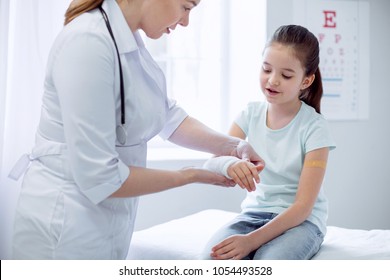 Broken Arm. Charming Smart Interested Girl Broking Arm And Female Doctor Putting Plaster While Standing