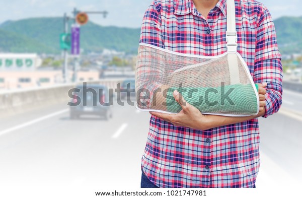 broken arm with green cast and arm sling\
isolated on blurred cars run on a Japanese highway with mountain\
background, insurance\
concept.