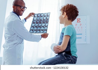 Broken Arm. Positive Friendly Doctor Standing Near The Light While Looking At His Patients Xray Image