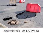 Broken asphalt near a manhole. The asphalt in the parking lot has collapsed near a rusty manhole cover where voids have formed.