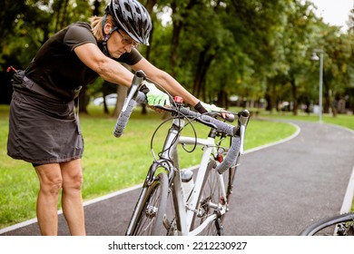 Broken bike while riding in the Park. Senior female have trouble with bicycle outdoor. Sporty Mature Woman cyclist fixing her bike - Powered by Shutterstock