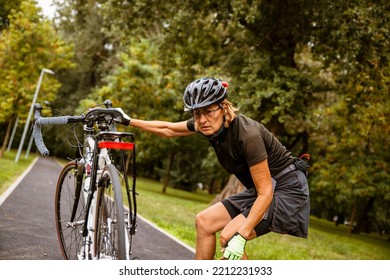 Broken Bike While Riding In The Park. Senior Female Have Trouble With Bicycle Outdoor. Sporty Mature Woman Cyclist Fixing Her Bike