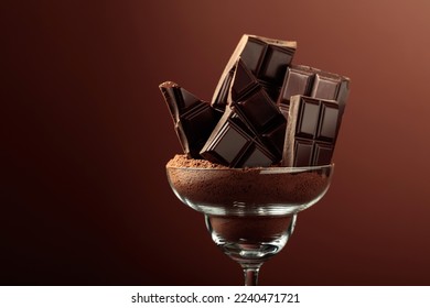 Broken black chocolate bar in glass with cocoa powder. Chocolate on a brown background with copy space.