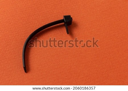 Broken black plastic cable tie on orange background