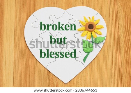 Broken but Blessed text on a white puzzle heart with a flower on wood for hope and faith