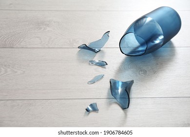 Broken blue glass vase on wooden floor. Space for text