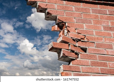 Broken brick wall and blue sky with clouds.