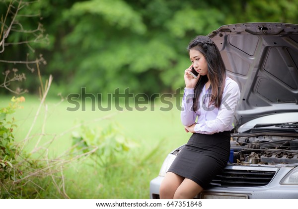 Broken car with businesswoman is using the\
phone to call a car\
mechanic.