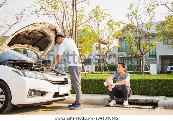 broken car\
calling for help on cell phone. broken car on the road. asian man\
and woman near broken car\
outdoors.