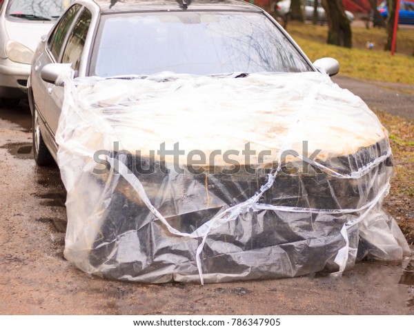 A broken car color silver, wrapped in a plastic\
coating. The car is covered with polyethylene after the accident.\
It is very debt.