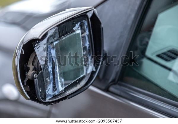 a broken car mirror repaired\
with adhesive tape and a small square mirror on a passenger\
car