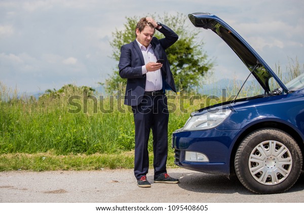 A broken car on the road, the\
driver is holding his head, an open hood, a car in\
failure