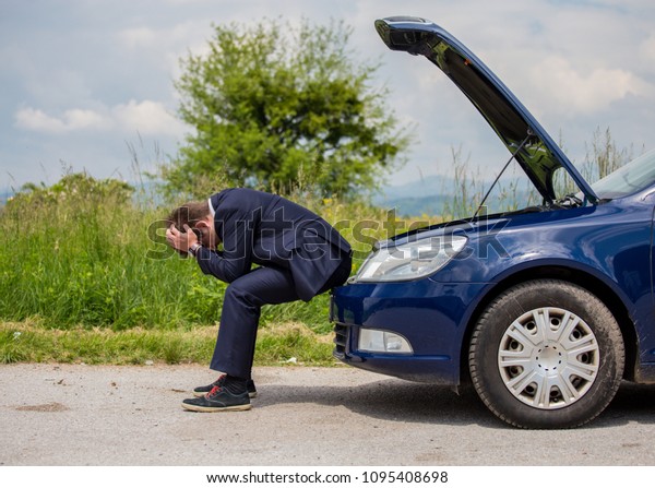 A broken car on the road, the
driver is holding his head, an open hood, a car in
failure