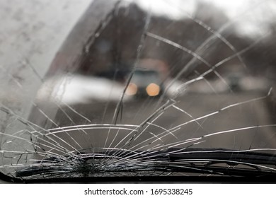 Broken car windshield - many cracks. Cloudy, outside blurred (defocused) car with luminous headlights. Inside view of the car - Shutterstock ID 1695338245