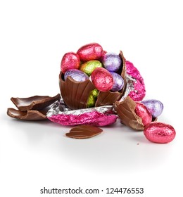 Broken Chocolate Easter Egg Wrapped In Pink Foil With Colorful Candies On White Background