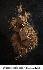 Broken chocolate pieces and cocoa powder on black. Chunks of chocolate onr dark stone background. - Shutterstock ID 1101931226