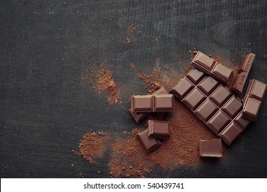 Broken chocolate pieces and cocoa powder on wooden background - Shutterstock ID 540439741
