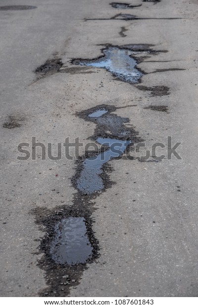 Broken city asphalt road with a lot of pits.\
Depressive urban\
landscape.