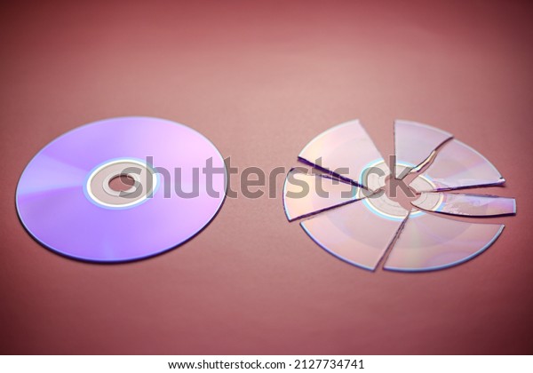 Broken compact disc divided into parts and a whole\
compact disc close-up on a red-burgundy background, complete loss\
of data