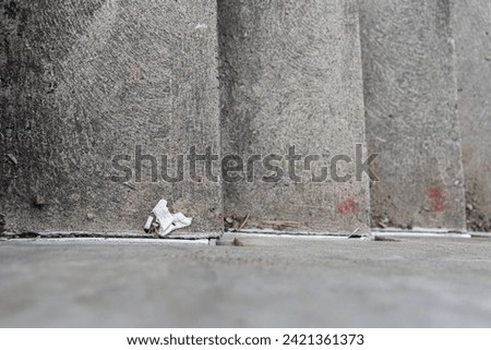 Broken concrete wall with a white piece of plastic in the corner and butch cigarette. Selective focus and shallow depth of field.