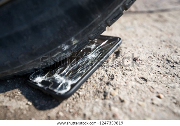 Broken and damaged smartphone with\
cracks on glass screen laying on ground. Accident. Cell phone under\
car wheel. Concept of warranty and lost smartphone\
\
