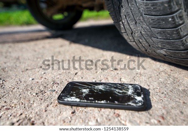 Broken and damaged smartphone with\
cracks on glass screen laying on ground. Accident. Cell phone under\
car wheel. Concept of warranty and lost smartphone\
\
