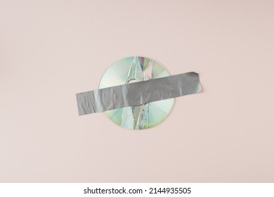 Broken digital audio compact disc tapped together with gray duct tape on pink background. - Shutterstock ID 2144935505