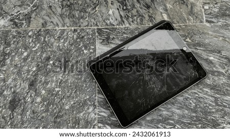 Broken digital tablet with cracked screen lying on a textured marble floor with copy space, representing technology mishaps or repair services