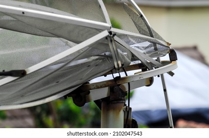 broken dish antenna. Mesh satellite dish with house building background. steel frame with broken lattice and posts. receiving antenna for receiving television or radio waves or telecommunications netw