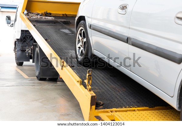 Broken down car being towed onto\
flatbed tow truck with cable for repair at workshop\
garage
