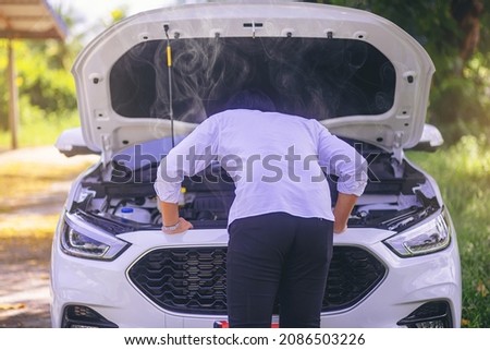 A broken down car, engine open and smoking, serious driver looking at the engine and do nothing. Selected focus