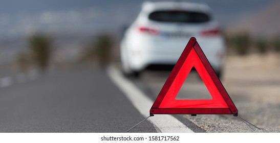 Broken down car with warning triangle behind it waiting for assistance to arrive, red triangle of a car on the road