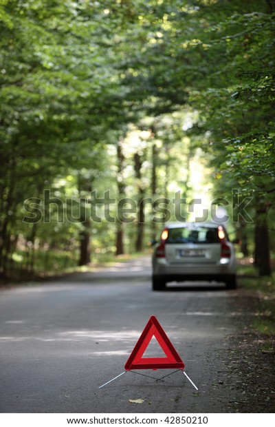 broken down car with warning\
triangle behind it waiting for assistance to arrive (shallow depth\
of field, the focus is on the triangle, the car is left out of\
focus)