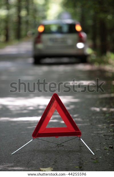 broken down car with warning\
triangle behind it waiting for assistance to arrive (shallow depth\
of field, the focus is on the triangle, the car is left out of\
focus)