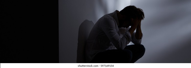 Broken down lonely young man sitting alone in the darkness - Shutterstock ID 597169154