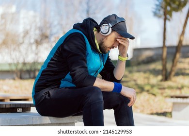 A Broken Down Sad Tired Man Is Not Happy With Workout Results. Runner Rests On A Wall In The Park, Covers Face With Hand, Low Motivation, Decline In Fitness.