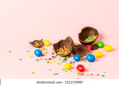 Broken Easter chocolate egg and multi-colored sweets on a pink background. Easter celebration concept.