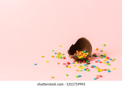 Broken Easter chocolate egg and multi-colored sweets on a pink background. Easter celebration concept.