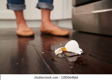 A Broken Egg On The Kitchen Floor After A Small Cooking Accident, Feet In The Background, Low Angle