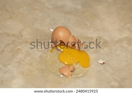 Broken egg with shell fragments and raw yolk on a light marble countertop, showcasing a domestic mishap.